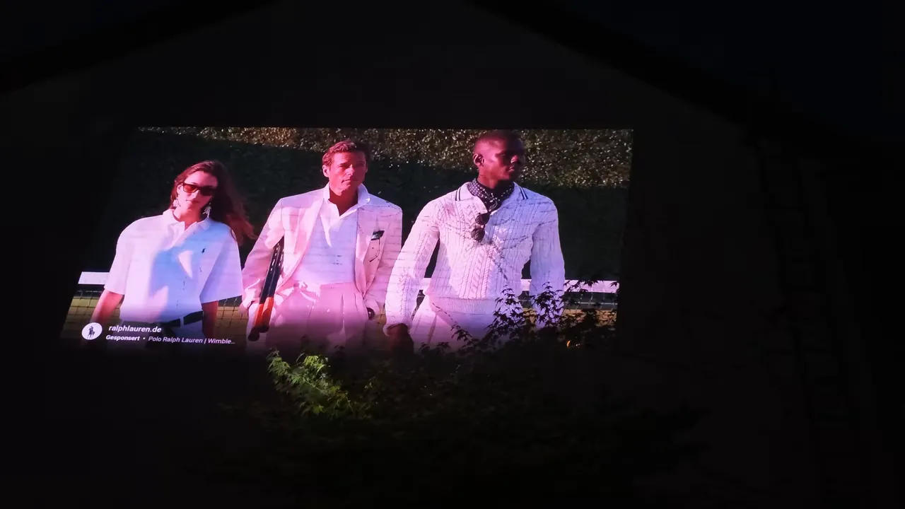 Mehrere helle Film- und Sportbilder auf einer großen Hauswand im Dunkeln
