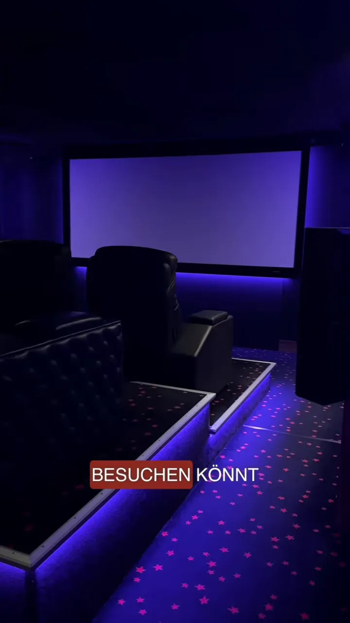 Dunkles GROBI-Kino mit schwarzen Ledersesseln, großer Leinwand und violetter Beleuchtung