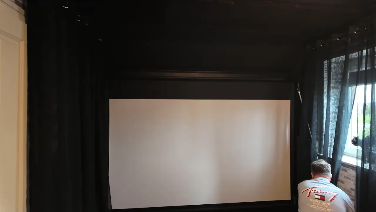 Heruntergelassene Leinwand zwischen schwarzen Vorhängen mit Lars an der manuellen Bedienung neben dem rechten Fenster