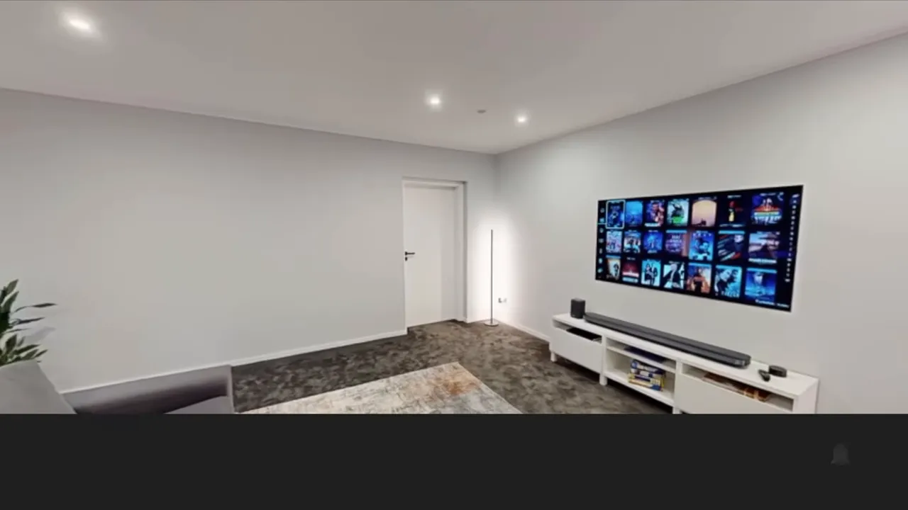 Wohnraum mit grauem Sofa, Fernseher, Soundbar und glatten weißen Wänden